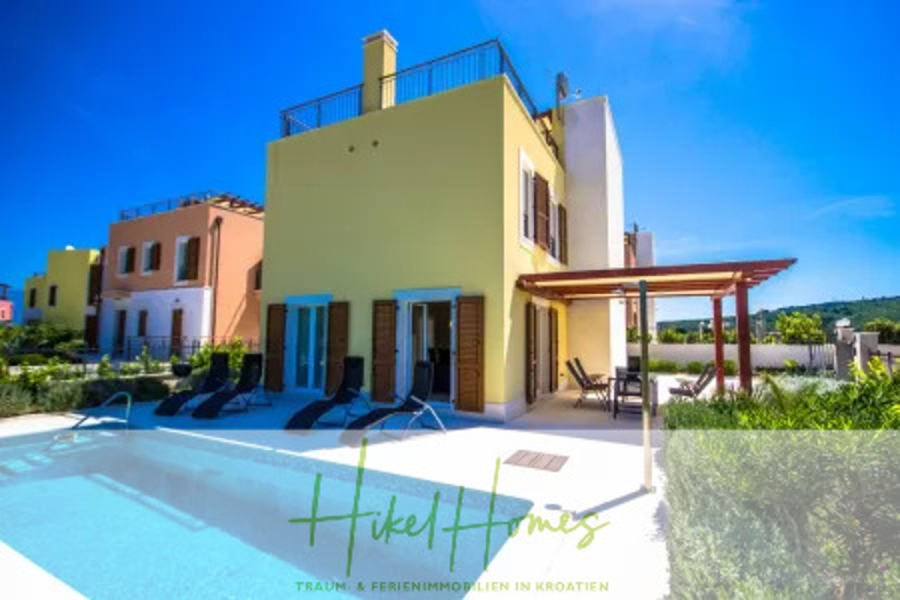 Villa im Mittelmeerstil mit 3 SZ, Pool, Dachterrasse mit Meerblick (2) - Eine moderne gelbe Villa mit blauen Fensterläden, einer schattigen Terrasse, Liegestühlen und einem Swimmingpool davor. Der Himmel ist klar und blau, und die Villa ist von Grün umgeben. Der Text "Hikel Homes" erscheint am unteren Rand. (44791)