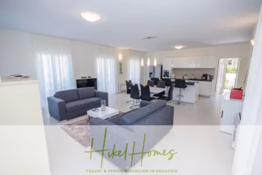 Villa im Mittelmeerstil mit 3 SZ, Pool, Dachterrasse mit Meerblick (2) - Großzügiger, offener Wohnbereich mit grauen Sofas, einem an der Wand montierten Fernseher und einem Esstisch mit schwarzen Stühlen. Der Raum ist dank großer Fenster gut beleuchtet, und im Hintergrund ist die Küche sichtbar. (41875)