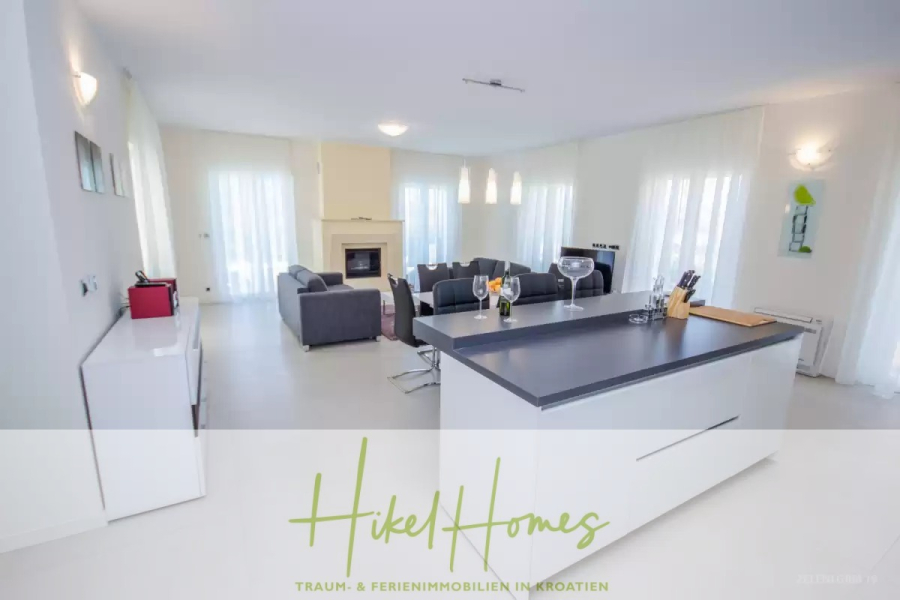 Villa im Mittelmeerstil mit 3 SZ, Pool, Dachterrasse mit Meerblick (2) - Moderner offener Wohnbereich mit einer Kücheninsel, grauen Sofas, einem Kamin und großen Fenstern mit transparenten Vorhängen. Helle, minimalistische Einrichtung mit weißen Wänden und viel natürlichem Licht. Die Textüberlagerung lautet "Hikel Homes". (44803)