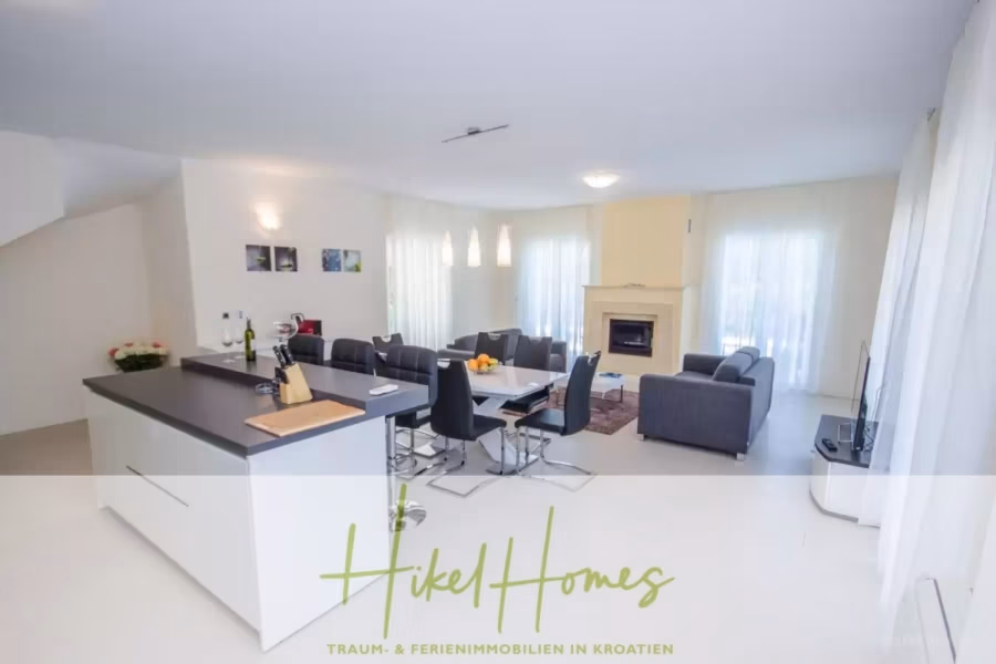 Villa im Mittelmeerstil mit 3 SZ, Pool, Dachterrasse mit Meerblick (2) - Geräumiges Wohnzimmer mit modernem Design, Esstisch, Sofas und Kamin. Der Raum verfügt über große Fenster mit transparenten Vorhängen. Im Vordergrund steht eine Kücheninsel. Die Einrichtung ist hell und luftig, in neutralen Farben gehalten. (41876)