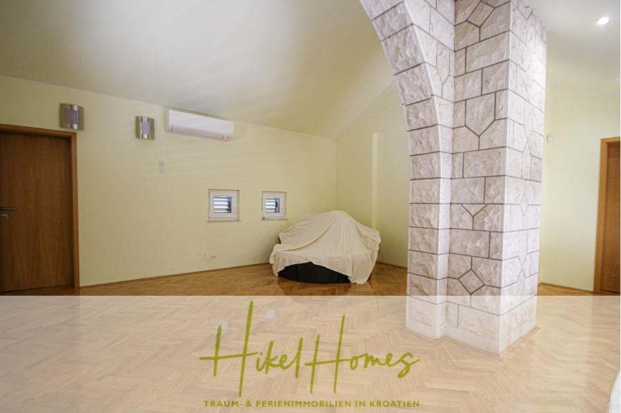 300m² Villa in 2. Reihe zum Meer mit großem Grundstück mit Erweiterungspotential - Geräumiger Raum mit hellgelben Wänden, Holzfußboden, einer großen Steinsäule, zwei Holztüren, zwei kleinen Fenstern und einem überdachten Möbelstück an der Rückwand. Logo "Hikel Homes" am unteren Rand. (44976)