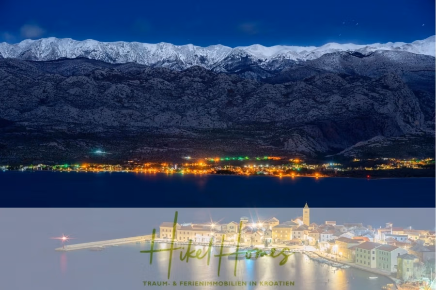 Luxus-Meerblick und Gebirgsblick-Villa in 2. Reihe zum Meer mit 4 SZ, Pool, Sauna, Fitness & Jacuzzi - Malerische Nachtansicht einer Küstenstadt in Kroatien. Die Stadt ist entlang der Uferpromenade unter einem Sternenhimmel beleuchtet, im Hintergrund schneebedeckte Berge. Der Text „Hikel Homes – Traum- & Ferienimmobilien in Kroatien“ wird angezeigt. (42070)