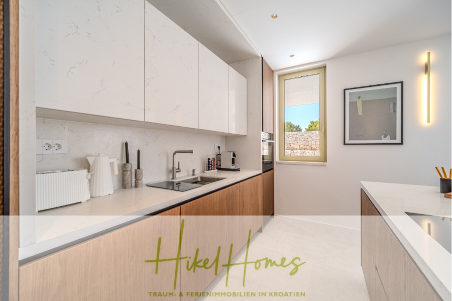 Hochwertige Meerblick Villa SUN in Sutivan (Insel Brac) – 3 SZ + Bad, Pool, Sommerküche, WC, … - Moderne, minimalistische Küche mit weißen und hölzernen Schränken, Arbeitsflächen aus Marmor, Spüle, Kaffeemaschine und einem Fenster, das natürliches Licht hereinlässt. Ein gerahmtes Bild und eine vertikale Leuchte zieren die Wand. (44988)