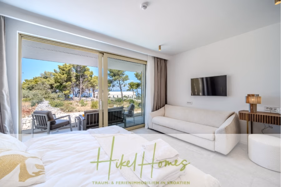 Hochwertige Meerblick Villa SUN in Sutivan (Insel Brac) – 3 SZ + Bad, Pool, Sommerküche, WC, … - Modernes Schlafzimmer mit großem Bett, weißem Sofa, Wandfernseher und Blick durch Glasschiebetüren auf eine möblierte Terrasse und Bäume im Freien. Das Zimmer ist hell und luftig und minimalistisch eingerichtet. (42973)