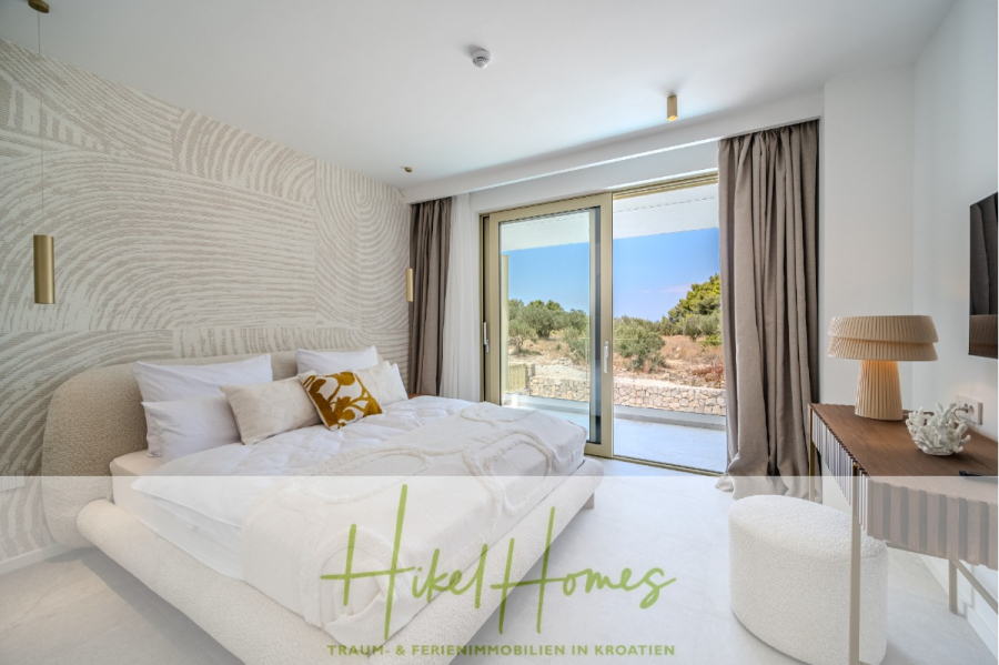 Hochwertige Meerblick Villa SUN in Sutivan (Insel Brac) – 3 SZ + Bad, Pool, Sommerküche, WC, … - Modernes, helles Schlafzimmer mit einem großen Bett, dekorativen Kissen, strukturierten Wänden und Glasschiebetüren, die auf einen Balkon mit Blick ins Freie führen. Ein Schreibtisch, eine Lampe und helle Vorhänge vervollständigen den minimalistischen, luftigen Raum. (44993)