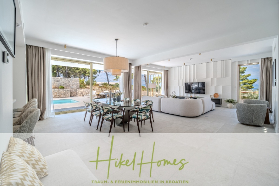Hochwertige Meerblick Villa SUN in Sutivan (Insel Brac) – 3 SZ + Bad, Pool, Sommerküche, WC, … - Moderner, geräumiger Wohn- und Essbereich mit großen Fenstern mit Blick auf eine Terrasse und einen Pool, hellen Möbeln, einem stilvollen Kronleuchter und neutralen Farben. Das Logo "Hikel Homes" und deutscher Text erscheinen am unteren Rand. (44989)