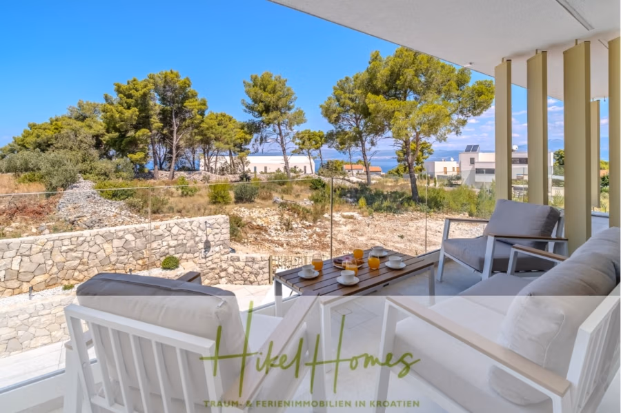 Hochwertige Meerblick Villa SUN in Sutivan (Insel Brac) – 3 SZ + Bad, Pool, Sommerküche, WC, … - Eine sonnendurchflutete Terrasse mit weißen Möbeln bietet Ausblick auf eine ruhige Landschaft mit Pinien und weit entfernten Häusern. Ein Tisch ist mit Orangensaft und Bechern gedeckt. Ein Glasgeländer bietet einen ungehinderten Blick auf die Natur unter einem klaren blauen Himmel. (42972)