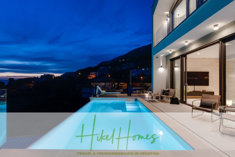 Sofort einziehen! Meerblick Villa CECILIE Infinity Pool, 3 SZ, Sommerküche, Videoraum mit PS5, …. - Moderne Villa mit beleuchtetem Pool und Außensitzplätzen in der Abenddämmerung mit Blick auf Hügel und ein Dorf unter dramatisch blauem Himmel. Texteinblendung: „Hikel Homes – Traum- & Ferienimmobilien in Kroatien.“. (43923)