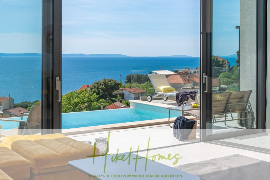 Sofort einziehen! Meerblick Villa CECILIE Infinity Pool, 3 SZ, Sommerküche, Videoraum mit PS5, …. - Eine sonnige Terrasse mit Pool bietet Blick auf das Meer und die Dächer der kroatischen Küste. Loungesessel und ein gelbes Sofa laden zum Entspannen ein. Glastüren rahmen den malerischen Ausblick ein. Unten befindet sich der Schriftzug „Hikel Homes“. (43913)