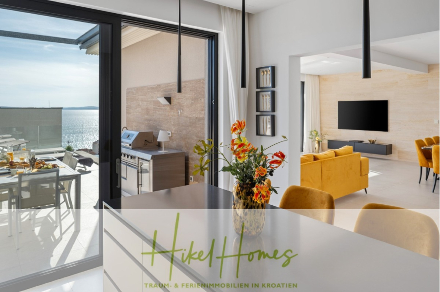 Sofort einziehen! Meerblick Villa CECILIE Infinity Pool, 3 SZ, Sommerküche, Videoraum mit PS5, …. - Moderner, offener Wohnbereich mit Essbereich, gelben Sofas und Fernseher. Große Glastüren führen auf die Terrasse mit Esstisch, Grill und Meerblick. Der Text lautet: „Hikel Homes Traum- & Ferienimmobilien in Kroatien.“. (43906)