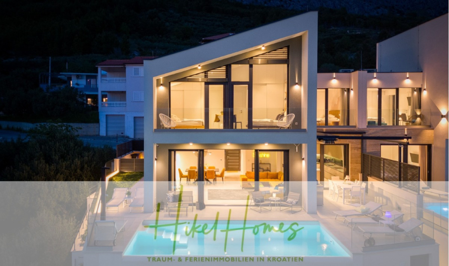 Sofort einziehen! Meerblick Villa CECILIE Infinity Pool, 3 SZ, Sommerküche, Videoraum mit PS5, …. - Eine moderne, beleuchtete Villa mit großen Fenstern, Balkonen und Pool in der Abenddämmerung. Berge und Grün bilden die Kulisse. Das Logo „Hikel Homes“ und der Text „Traum- & Ferienimmobilien in Kroatien“ sind unten eingeblendet. (43918)