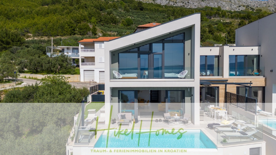 Sofort einziehen! Meerblick Villa CECILIE Infinity Pool, 3 SZ, Sommerküche, Videoraum mit PS5, …. - Eine moderne Villa mit großen Glasfenstern, einem einzigartigen Winkeldach, einem Swimmingpool und Liegestühlen im Freien, eingebettet in einen Hügel in Kroatien. Der Text „Hikel Homes Traum- & Ferienimmobilien in Kroatien“ ist eingeblendet. (43892)