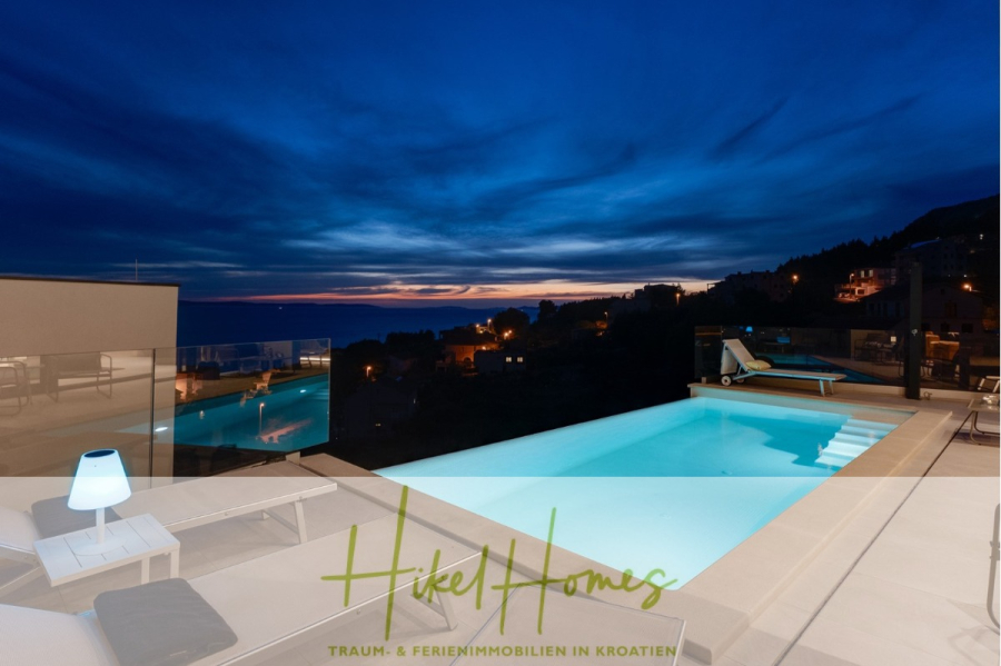 Sofort einziehen! Meerblick Villa CECILIE Infinity Pool, 3 SZ, Sommerküche, Videoraum mit PS5, …. - Luxusvilla mit modernem Außenpool, Liegestühlen und Glasgeländer mit Blick auf eine Küstenstadt bei Sonnenuntergang unter dramatisch blauem und orangefarbenem Himmel. Unten steht der Text „Hikel Homes Traum- & Ferienimmobilien in Kroatien“. (43919)