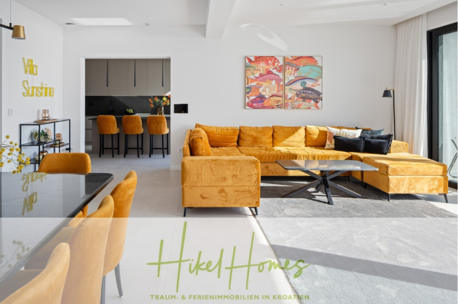 Sofort einziehen! Meerblick Villa CECILIE Infinity Pool, 3 SZ, Sommerküche, Videoraum mit PS5, …. - Moderner Wohnraum mit senfgelbem Sofa, Esstisch und Stühlen, Küche mit Barhockern, farbenfroher Wandkunst und großen Fenstern, die natürliches Licht hereinlassen. „Hikel Homes“-Logo und Textüberlagerung unten. (43917)