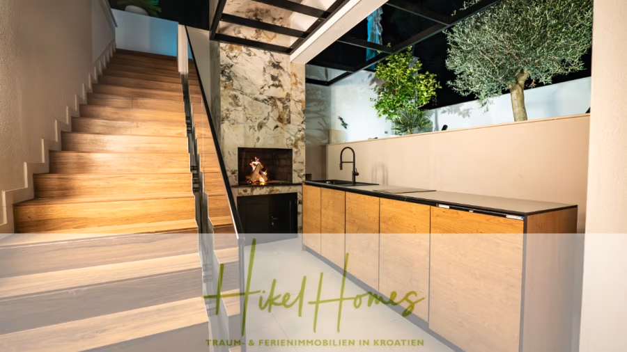 Luxus trifft Meerblick – Ein Anwesen der Extraklasse – Sofort einziehen - Stilvoller Innenbereich mit Holztreppe nach oben, angrenzend an eine moderne Küchenzeile. Der Raum besticht durch sein minimalistisches Design mit natürlichem Dekor, darunter ein Baum und Grünpflanzen im Hintergrund, die die erdfarbenen Möbel ergänzen. (43750)