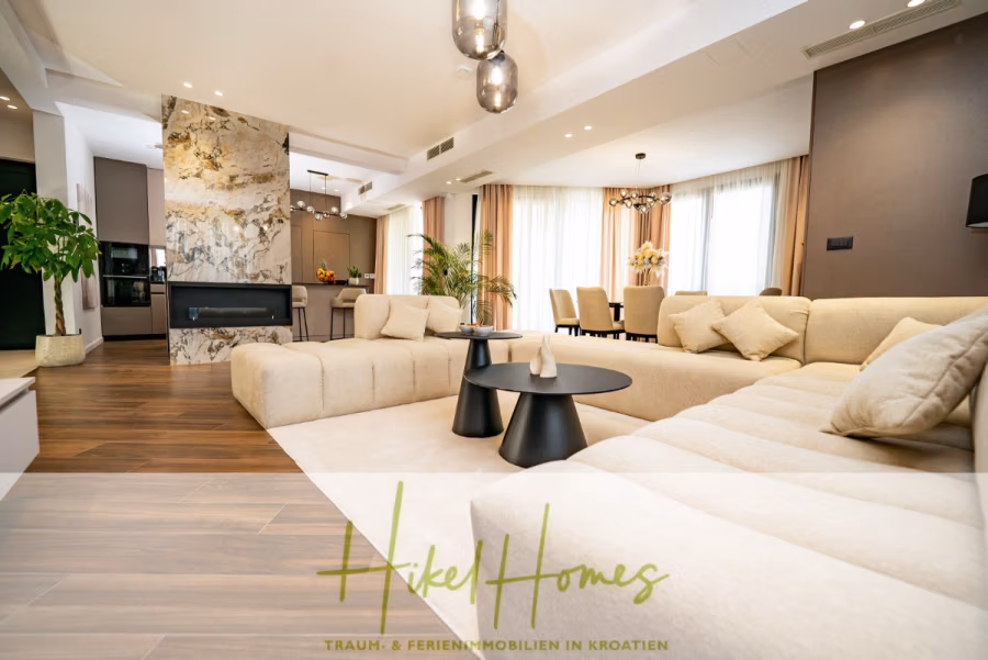 Luxus trifft Meerblick – Ein Anwesen der Extraklasse – Sofort einziehen - Geräumiges, modernes Wohnzimmer mit einem großen beigefarbenen Sofa, runden schwarzen Couchtischen und einer Marmor-Akzentwand. Im Hintergrund ist ein Essbereich mit gepolsterten Stühlen und großen Fenstern zu sehen, die viel Tageslicht hereinlassen. (43743)