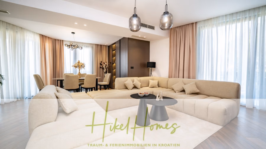 Luxus trifft Meerblick – Ein Anwesen der Extraklasse – Sofort einziehen - Geräumiges, modernes Wohnzimmer mit einem großen beigefarbenen Sofa und einem runden schwarzen Couchtisch. Im Hintergrund befindet sich ein Essbereich mit Tisch und Stühlen. Drei Pendelleuchten hängen von der Decke. Helle Vorhänge verdecken die Fenster. (43742)
