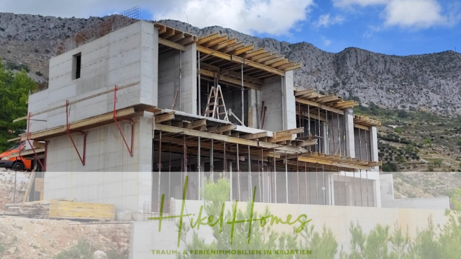 Schlüsselfertige – großzügige Meerblick Villa in ruhiger Lage, 4 SZ, 4 Bäder, Pool, Jacuzzi, … - Ein modernes, im Bau befindliches Betonhaus an einem Hang, mit Gerüsten und sichtbaren Holzbalken, vor einem Hintergrund aus felsigen Bergen und einem teilweise bewölkten Himmel. Das Logo "Hike Homes" ist am unteren Rand eingeblendet. (45356)