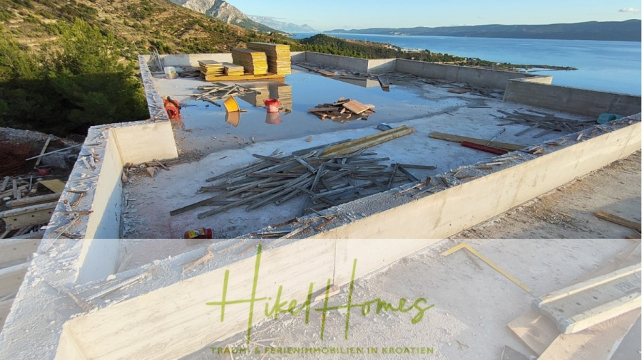 Schlüsselfertige – großzügige Meerblick Villa in ruhiger Lage, 4 SZ, 4 Bäder, Pool, Jacuzzi, … - Ein im Bau befindliches Betonfundament an einem Hang, mit verstreuten Materialien und Werkzeugen, mit Blick auf das Meer und die Berge in Kroatien. Das Logo und der Slogan von "Hikel Homes" erscheinen am unteren Rand. (45354)