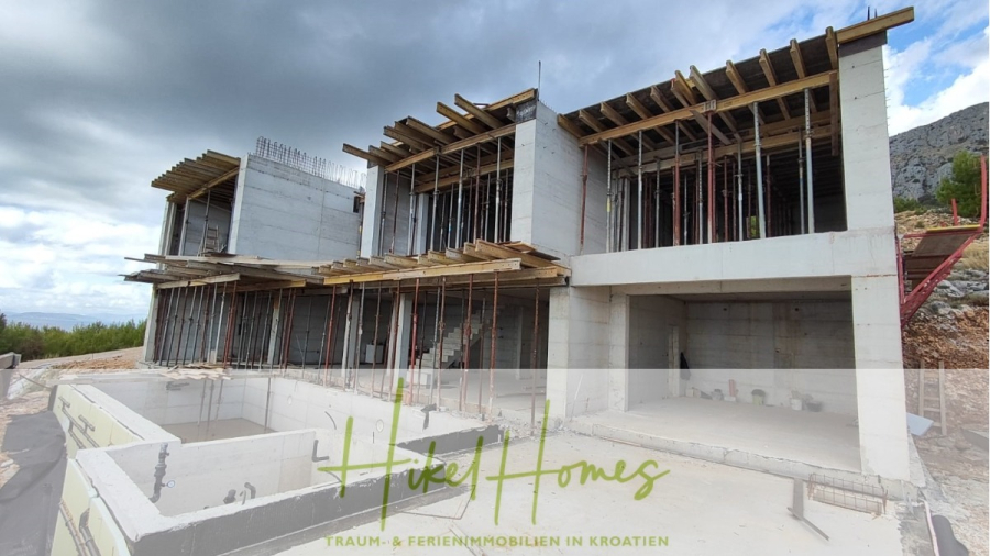 Schlüsselfertige – großzügige Meerblick Villa in ruhiger Lage, 4 SZ, 4 Bäder, Pool, Jacuzzi, … - Ein modernes, im Bau befindliches Betongebäude steht an einem Hang, mit freiliegenden Balken und Gerüsten. Im Vordergrund ist ein unfertiger Pool zu sehen. Das Logo "Hikel Homes" mit deutschem Text überlagert das Bild. (45357)