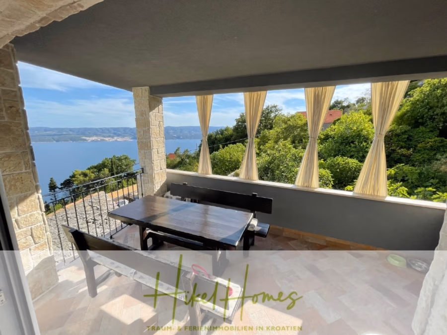 Meerblick aus perfekter Höhenlage mit 3 Schlafzimmern - Überdachte Terrasse mit Esstisch und Bänken und Blick auf die Küste. Die Terrasse ist von Steinsäulen eingerahmt und mit gelben Vorhängen geschmückt. Im Hintergrund sind Grünflächen und das Meer zu sehen. Der Logotext unten lautet „Hikel Homes“. (41482)