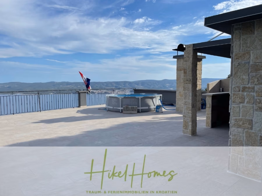Meerblick aus perfekter Höhenlage mit 3 Schlafzimmern - Dachterrasse mit Steinfassade, teilweisem Meerblick und aufblasbarem Pool. Die kroatische Flagge weht neben einem kleinen Barbereich. In der Ferne sind Hügel unter blauem Himmel zu sehen. Der Text lautet: „Hikel Homes – Traum- & Ferienimmobilien in Kroatien.“. (41475)