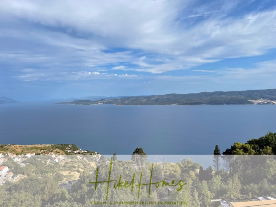 Meerblick aus perfekter Höhenlage mit 3 Schlafzimmern - Ein malerischer Blick auf eine Küstenlandschaft mit weitem blauem Wasser unter leicht bewölktem Himmel. Im Vordergrund sind Bäume und eine kleine Gebäudegruppe auf einem Hügel zu sehen. Unten ist der Text „HikeHomes“ eingeblendet. (41479)