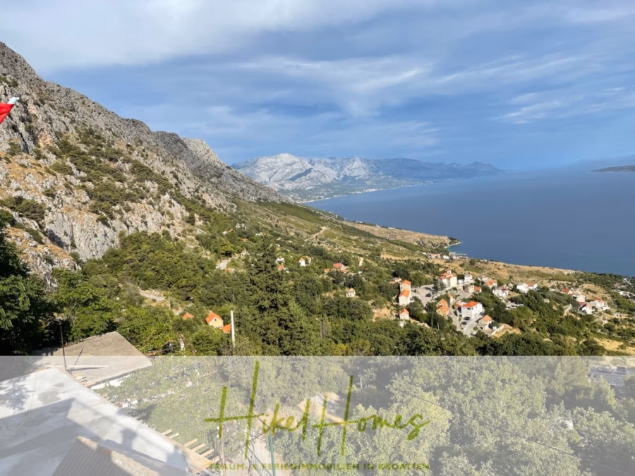 Meerblick aus perfekter Höhenlage mit 3 Schlafzimmern - Ein malerischer Blick auf eine Küstenregion mit Bergen, einem felsigen Hang und einer Ansammlung kleiner Häuser im Grünen. Das Meer erstreckt sich unter einem teilweise bewölkten Himmel bis zum Horizont. (41489)