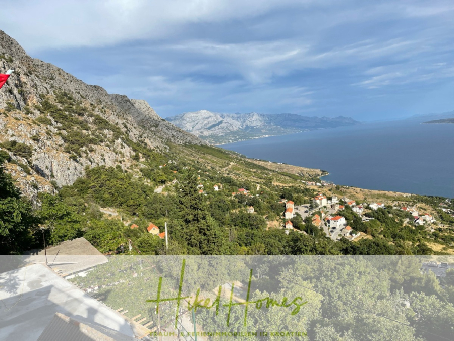 Meerblick aus perfekter Höhenlage mit 3 Schlafzimmern - Eine malerische Küstenlandschaft mit zerklüfteten Bergen, einer Ansammlung von Häusern mit roten Dächern, grüner Vegetation und einem ruhigen blauen Meer unter einem teilweise bewölkten Himmel. (46090)