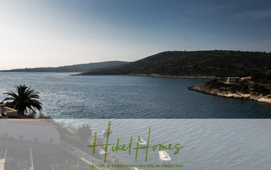 Villa Ana – 250m² WFL in 1. Reihe zum Meer / 4 SZ / Neubau / Sofort bezugsfertig - Eine ruhige Küstenszene in Kroatien zeigt blaues Wasser, eine Palme, Hügel und eine kleine Anlegestelle mit Booten. Der Text "Hikel Homes - Traum Ferienimmobilien in Kroatien" ist am unteren Rand eingeblendet. (46528)