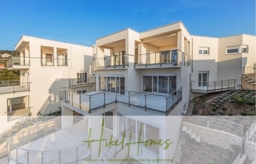 Villa Ana – 250m² WFL in 1. Reihe zum Meer / 4 SZ / Neubau / Sofort bezugsfertig - Moderne mehrstöckige Gebäude mit Balkonen und großen Fenstern in einem Wohngebiet, umgeben von einem angelegten Garten. Das Bild zeigt unten ein Logo und Text zum Thema Immobilien in Kroatien. (41548)