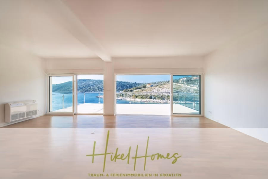 Villa Ana – 250m² WFL in 1. Reihe zum Meer / 4 SZ / Neubau / Sofort bezugsfertig - Minimalistisches Zimmer mit großen Fenstern und malerischem Blick auf das blaue Meer und die bewaldeten Hügel. Der Raum hat Holzboden und weiße Wände. Der Text unten lautet: „Hikel Homes – Traum- & Ferienimmobilien in Kroatien.“. (41541)