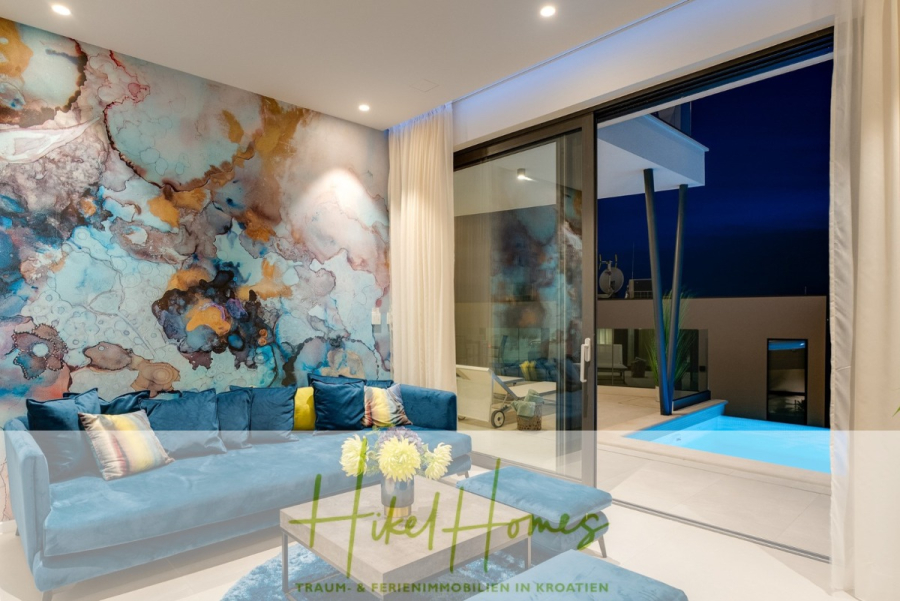 Direkt einziehen Meerblick Villa NATALIA mit Infinity Pool, 3 SZ, Sommerküche, … - Modernes Wohnzimmer mit lebendigem abstraktem Wandbild, blauem Samtsofa und Glastüren, die nachts auf eine Terrasse mit Pool führen. Der Innenraum ist stilvoll und hell erleuchtet und verbindet Innen- und Außenbereich. (43878)