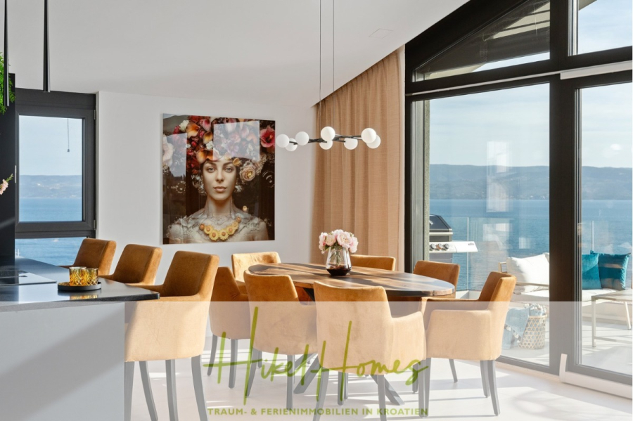 Direkt einziehen Meerblick Villa NATALIA mit Infinity Pool, 3 SZ, Sommerküche, … - Moderner Essbereich mit hellbraunen Stühlen um einen Holztisch, zeitgenössischer Beleuchtung, großem Wandbild einer Frau mit Blumen, raumhohen Fenstern und Meerblick. Unten befindet sich der Logotext „Hikes Homes“. (43865)