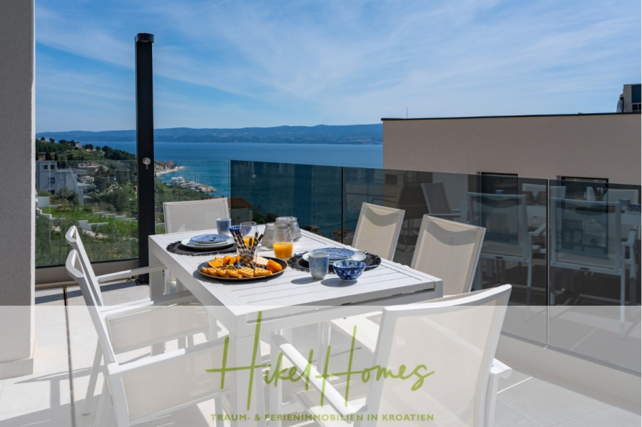 Direkt einziehen Meerblick Villa NATALIA mit Infinity Pool, 3 SZ, Sommerküche, … - Ein moderner Essbereich im Freien auf einem Balkon bietet Blick auf das Meer und die Küste. Ein Tisch ist mit Frühstücksspeisen und Getränken gedeckt, umgeben von weißen Stühlen, unter einem blauen Himmel mit fernen Hügeln und ruhigem Wasser. (43861)