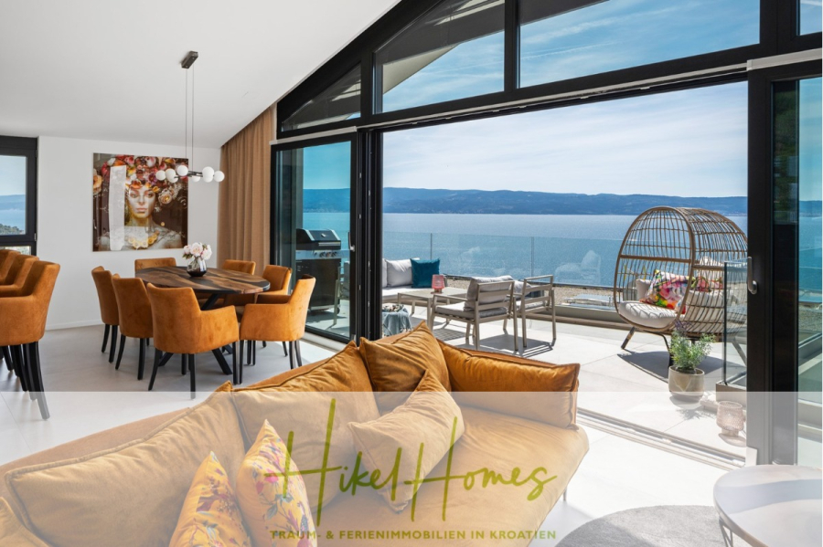 Direkt einziehen Meerblick Villa NATALIA mit Infinity Pool, 3 SZ, Sommerküche, … - Moderner Wohn- und Essbereich mit orangefarbenen Stühlen, großen Fenstern und Meerblick. Ein Balkon mit Sitzgelegenheiten bietet Blick aufs Wasser. Kunstwerke schmücken die Wand. Der Logotext lautet: „Hikel Homes – Traum- & Ferienimmobilien in Kroatien.“. (43868)