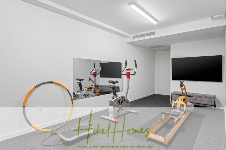 Direkt einziehen Meerblick Villa NATALIA mit Infinity Pool, 3 SZ, Sommerküche, … - Ein modernes Home-Fitnessstudio mit Heimtrainer, Rudergerät, großem Wandspiegel, Hula-Hoop-Reifen, Flachbildfernseher sowie kleinem Tisch und Stuhl. Der Raum hat weiße Wände und einen grauen Teppich. (43881)