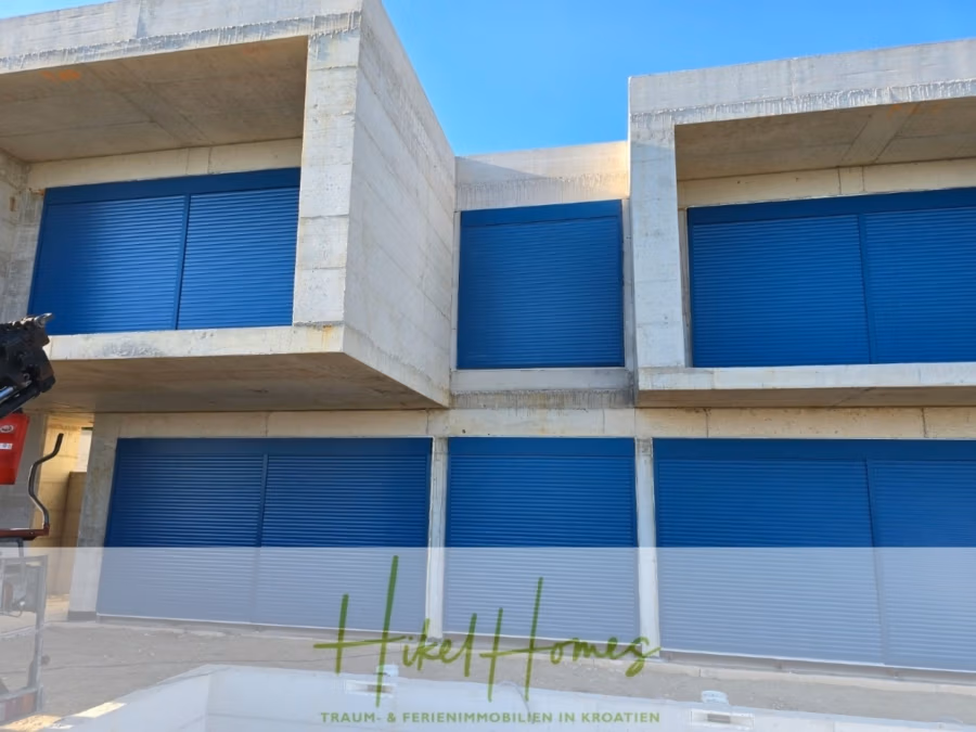 Schlüsselfertige – großzügige Meerblick Villa in ruhiger Lage, 4 SZ, 4 Bäder, Pool, … - Betongebäude mit blauen Rollläden vor den Fenstern und mehreren modularen Elementen. Unter dem Gebäude befindet sich das Logo „Hikel Homes“ mit dem Slogan „Traum- & Ferienimmobilien in Kroatien“. Links ist ein Baukran teilweise sichtbar. (42488)