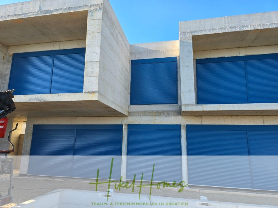 Schlüsselfertige – großzügige Meerblick Villa in ruhiger Lage, 4 SZ, 4 Bäder, Pool, … - Modernes Betongebäude mit vier großen blauen Garagenrolltoren, die jeweils in einer kastenartigen Struktur angeordnet sind. Logo "Hikel Homes" und Textüberlagerung am unteren Rand mit deutschen Worten über Immobilien in Kroatien. (45178)