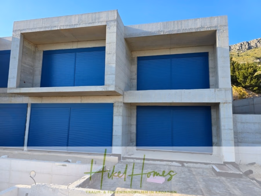 Schlüsselfertige – großzügige Meerblick Villa in ruhiger Lage, 4 SZ, 4 Bäder, Pool, … - Modernes dreistöckiges Gebäude mit blauen Rollläden vor jedem Fenster. Das Gebäude besteht aus Beton und liegt vor einer grünen Landschaft mit einem felsigen Hügel. Unten ist das Logo „Hikel Homes“ zu sehen. (42486)