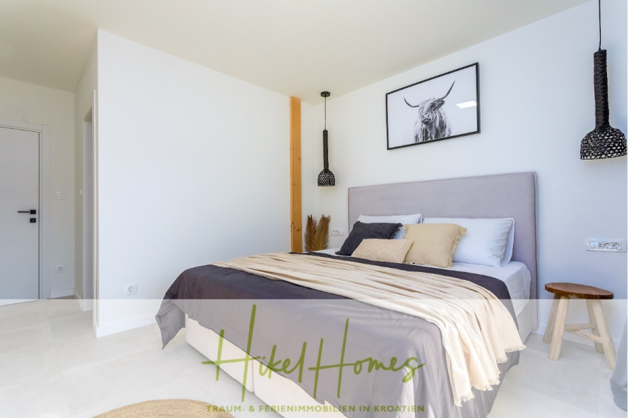 4 Schlafzimmer / 32m² Pool / Sommerküche – Neubauhaus nur 8km von Omis entfernt - Helles, modernes Schlafzimmer mit einem Doppelbett, neutraler Bettwäsche, zwei Hängelampen, einem gerahmten Bild einer Kuh über dem Kopfteil und minimalem Dekor. Logo und Text von "Hike Homes" überlagern den Boden. (44120)