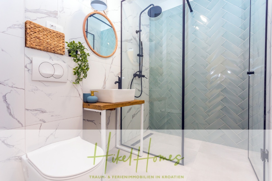 4 Schlafzimmer / 32m² Pool / Sommerküche – Neubauhaus nur 8km von Omis entfernt - Modernes Badezimmer mit Wänden mit Marmormuster, einer Glasdusche mit schwarzen Armaturen, einer hölzernen Arbeitsplatte mit weißem Waschbecken, einem runden Spiegel und einer Topfpflanze. Der Text am unteren Rand lautet "Hakel Homes". (44121)