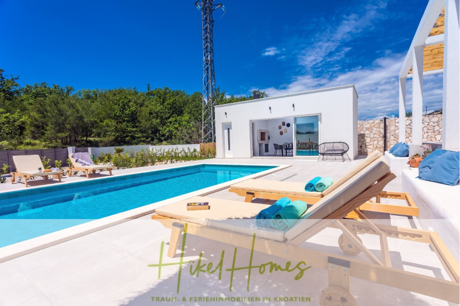 4 Schlafzimmer / 32m² Pool / Sommerküche – Neubauhaus nur 8km von Omis entfernt - Moderne Villa mit privatem Pool, Sonnenliegen mit Handtüchern und Sitzgelegenheiten auf der Terrasse vor üppigem Grün und blauem Himmel; das Logo und der Text von "Hikel Homes" erscheinen am unteren Rand des Bildes. (44110)