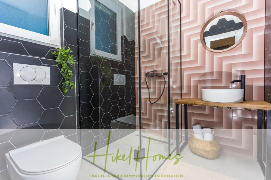 4 Schlafzimmer / 32m² Pool / Sommerküche – Neubauhaus nur 8km von Omis entfernt - Modernes Badezimmer mit schwarzen sechseckigen Fliesen, einer Glasdusche, einer rosafarbenen geometrischen Akzentwand, einer wandmontierten Toilette, einem runden Waschbecken auf einer hölzernen Arbeitsplatte und darunter gelagerten Handtüchern. Der Text des Logos lautet: "Hikel Homes. (44119)
