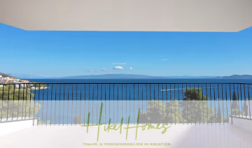 Ein geräumiger Balkon mit schwarzem Geländer bietet Aussicht auf das ruhige, blaue Meer, die Berge in der Ferne und einen Teil einer Küstenstadt unter klarem Himmel. Unten steht: „Hikel Homes Traum- & Ferienimmobilien in Kroatien.“. - Luxus Meerblick 77m² Ensemble mit 2 Schlafzimmern, Terrasse und Südausrichtung (1. OG)