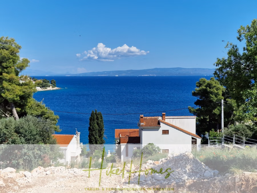 Luxus Meerblick 77m² Ensemble mit 2 Schlafzimmern, Terrasse und Südausrichtung (1. OG) - Blick auf ein leuchtend blaues Meer mit einigen weißen Häusern und roten Dächern im Vordergrund, umgeben von grünen Bäumen und in der Ferne Bergen unter einem teilweise bewölkten Himmel. (43850)