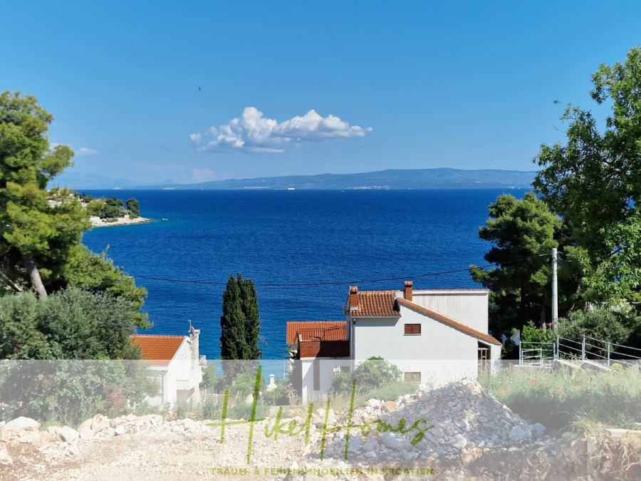Luxus Meerblick 77m² Ensemble mit 2 Schlafzimmern, Terrasse und Südausrichtung (1. OG) - Blick auf ein Küstendorf mit weißen Häusern und orangefarbenen Dächern, umgeben von Grün, mit Blick auf ein tiefblaues Meer unter einem klaren Himmel. Bäume und Hügel sind auf beiden Seiten und auf der anderen Seite des Wassers zu sehen. (46848)